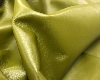 May include: Close-up of a piece of soft, green leather with a smooth, slightly textured surface. The leather is folded and draped, showing its flexibility and drape.