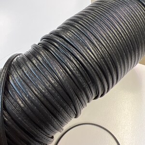 May include: A roll of black leather cord, wound tightly in a coil. The cord is smooth and has a subtle sheen.