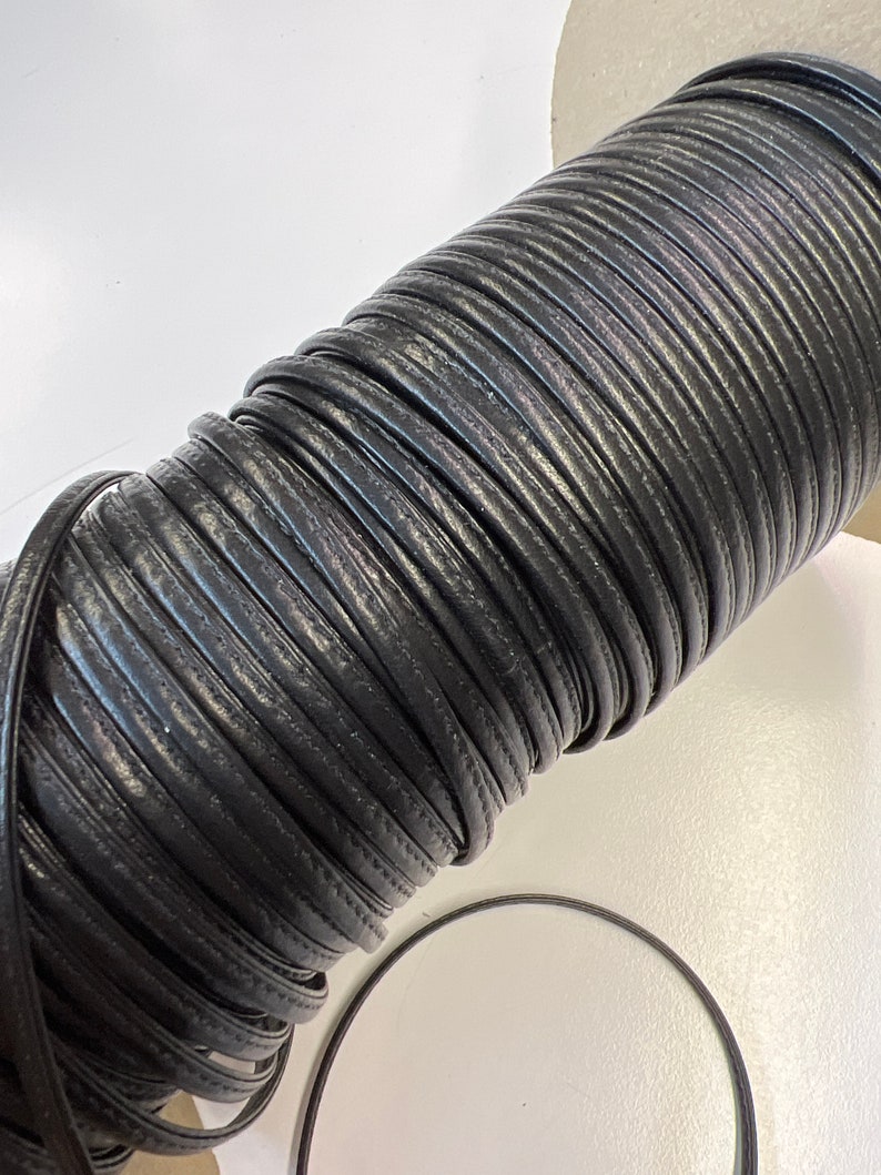 May include: A roll of black leather cord, wound tightly in a coil. The cord is smooth and has a subtle sheen.