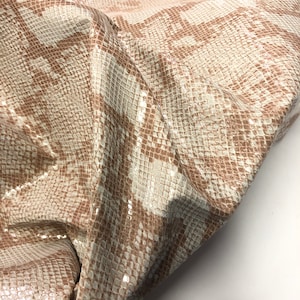 May include: Close-up of a beige snakeskin fabric with a subtle shimmer. The fabric has a textured pattern that resembles snake scales.