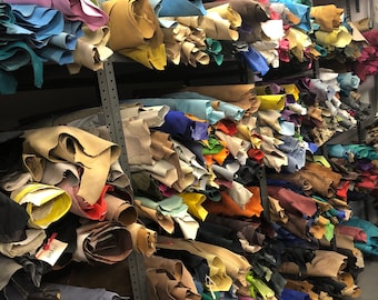 May include: A shelf filled with rolls of leather in various colors, including brown, blue, green, red, and yellow. The leather is stacked high on the shelves, creating a colorful and textured display.