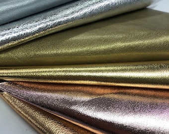 May include: A close-up of five different metallic leather swatches. The swatches are arranged in a fan shape, with the silver swatch on top and the gold swatch on the bottom. The swatches are all textured and have a metallic sheen.