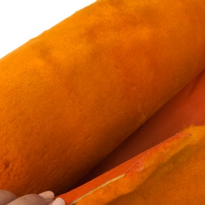 May include: A close-up of a roll of orange fabric with a soft, fuzzy texture. The fabric is folded in half, revealing a smooth, orange backing.
