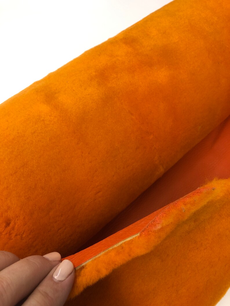 May include: A close-up of a roll of orange fabric with a soft, fuzzy texture. The fabric is folded in half, revealing a smooth, orange backing.