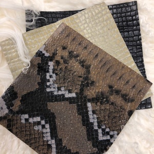 May include: Three different types of leather swatches: a black crocodile embossed leather, a light beige crocodile embossed leather, and a brown and black snakeskin leather.