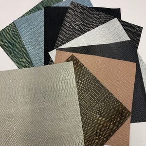 May include: Assortment of faux leather sheets in various colors and embossed textures, including green, blue, black, white, brown, and gold. The sheets are arranged in a fan shape, showcasing the different patterns and colors.