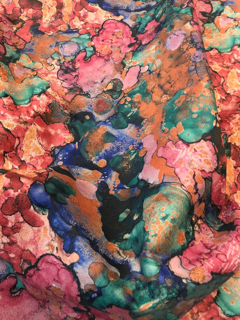May include: Abstract fabric with a colorful, marbled pattern in shades of pink, blue, green, and gold. The fabric has a soft, flowing texture.