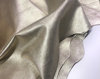 May include: A piece of metallic gold leather with a textured surface. The leather is folded and draped over a white surface.