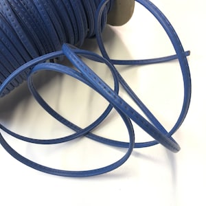 May include: A spool of blue leather cord with a stitched edge. The cord is coiled and ready to be used for crafting projects.