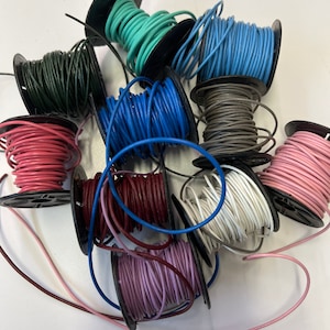 May include: Assortment of spools of colorful cord, including teal, blue, red, brown, white, pink, and purple. The cords are wound around black plastic spools.