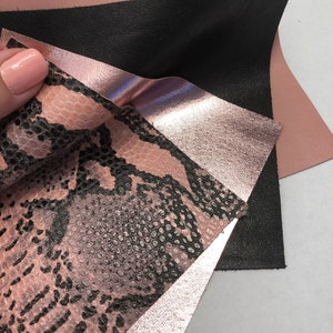 May include: Four pieces of leather in different colors and textures. The top piece is a light pink, the second piece is black, the third piece is a metallic rose gold, and the bottom piece is a pink snakeskin pattern.