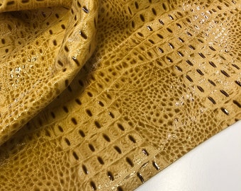 May include: A close-up of a piece of yellow faux leather with an alligator skin pattern. The leather is textured and has a glossy finish.
