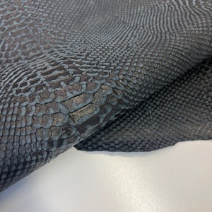 Puede incluir: Primer plano de una piel de serpiente gris oscuro con un patr&oacute;n texturizado. La piel est&aacute; doblada por la mitad, mostrando la parte inferior.