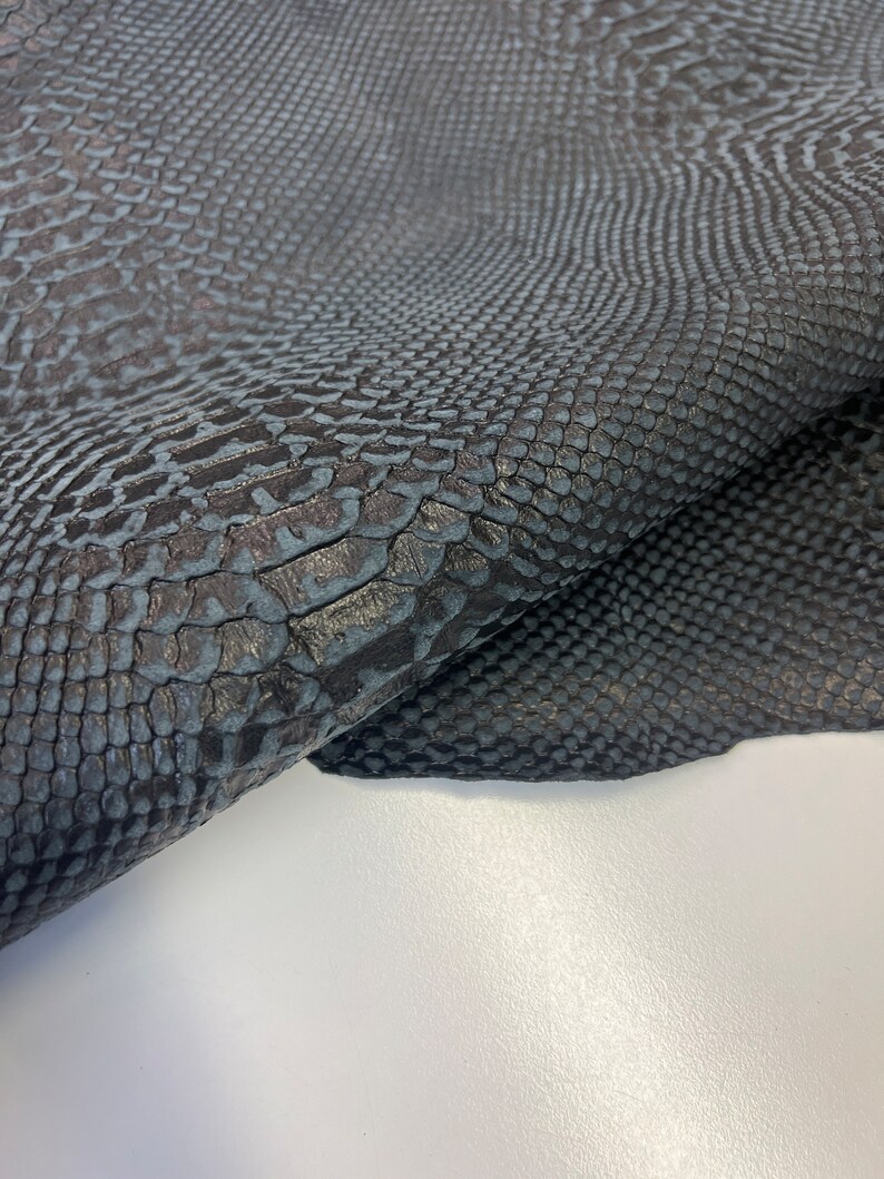 Puede incluir: Primer plano de una piel de serpiente gris oscuro con un patr&oacute;n texturizado. La piel est&aacute; doblada por la mitad, mostrando la parte inferior.