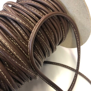 May include: A spool of brown leather cord with white stitching. The cord is wound tightly around the spool and is ready to be used for crafting projects.