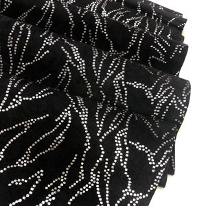 May include: Black fabric with a silver sparkly pattern of wavy lines. The fabric is folded in half.