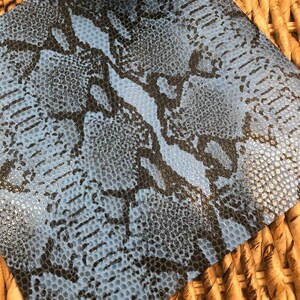 May include: A close-up of a blue and black snakeskin patterned fabric. The fabric has a textured surface and a subtle sheen.