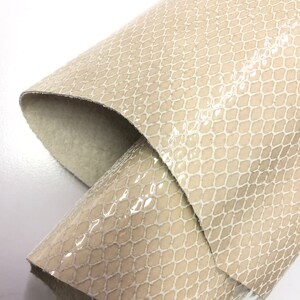 May include: A close-up of a beige snakeskin-embossed leather fabric. The fabric has a subtle sheen and a textured surface.