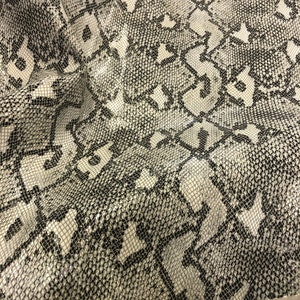 May include: Close-up of a white and black snakeskin pattern fabric. The fabric has a textured, woven look.