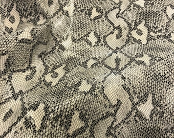 May include: Close-up of a white and black snakeskin pattern fabric. The fabric has a textured, woven look.