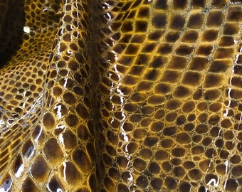 May include: Close-up of a piece of brown leather with a crocodile-embossed pattern. The leather has a glossy finish.