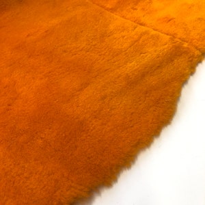 May include: Close-up of a piece of orange faux fur fabric. The fabric has a soft, fluffy texture.