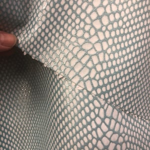 May include: Close-up of a light blue fabric with a white snakeskin pattern. The fabric has a subtle shimmer.