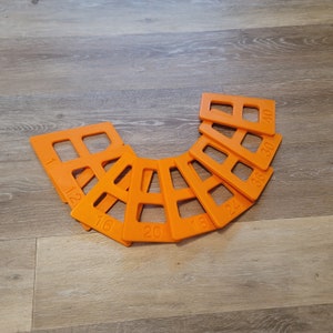 May include: A set of ten orange plastic tile spacers with numbers printed on them, ranging from 1 to 40. The spacers are arranged in a semi-circle.