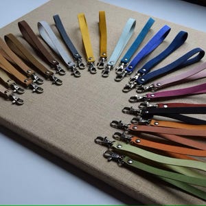 Puede incluir: Una colección de correas de muñeca de cuero en varios colores, incluyendo beige, marrón, amarillo, azul y verde. Cada correa tiene un cierre metálico para una fácil fijación. Las correas están dispuestas sobre una superficie de color neutro.
