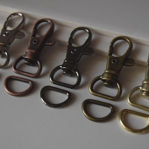 May include: An assortment of metal hardware, including five swivel clasps and five D-rings. The clasps and rings are in various metallic finishes: silver, copper, dark bronze, antique brass, and gold. Ideal for crafting and accessories.