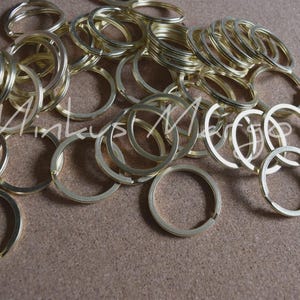 May include: A collection of gold-colored key rings scattered on a brown surface. The key rings are circular with a split ring design. The image includes the text "Mintkys Market" in a cursive font.