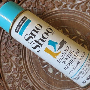 May include: Vintage Sno-Shoo silicone water repellent spray can for snow boots. The can is white with a light blue top and gold rim. The label features the brand name and illustrations of boots. Net weight 8 ounces.