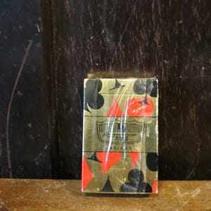 May include: A deck of playing cards in a gold and red design, featuring black clubs and red hearts. The card box is wrapped in clear plastic and sits on a wooden surface. The text on the box reads "BRIDGE".