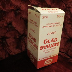 May include: A white and red box of "Glad Straws" with the text "Jumbo" and "250" printed on it. The box is 7 3/4 inches tall and is sitting on a red velvet surface. The box reads "Really Waterproof, Sanitary Too!" and "Ideal for all drinks."