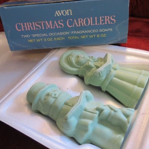 Może przedstawiać: Vintage mydła Avon Christmas Carolers. Mydła są jasnozielone i mają kształt kolędnika i bałwana. Pudełko jest turkusowe i ma napis "AVON CHRISTMAS CAROLLERS". Całkowita waga netto 170 gramów.