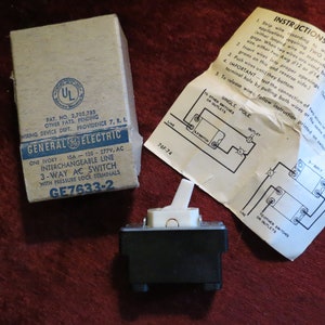 May include: A vintage General Electric 3-way AC switch with a white toggle and black base, accompanied by its original box and wiring instructions. The box is beige with blue text and the UL logo. The instructions are printed on a white paper.