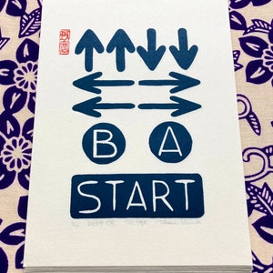 Peut inclure: Une impression blanche avec des flèches bleu marine, des boutons A et B, et le mot START. L'impression comprend le texte "2023年5月 THE CORE Takuma Shimizu" dans le coin inférieur.