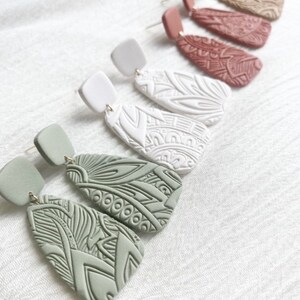 May include: A set of three pairs of dangle earrings with intricate geometric patterns. The earrings are made of clay and come in green, white, and red.
