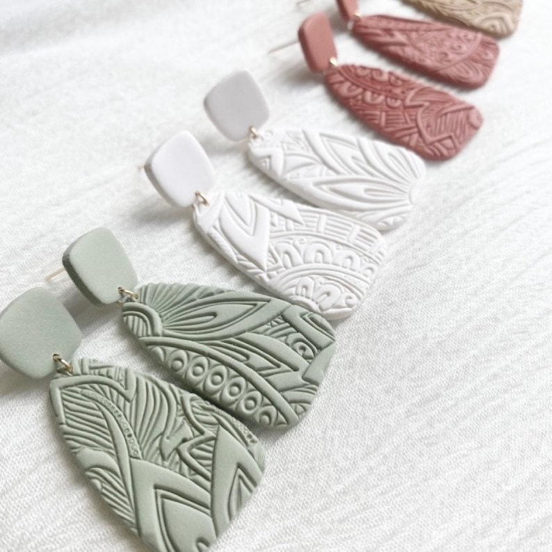 May include: A set of three pairs of dangle earrings with intricate geometric patterns. The earrings are made of clay and come in green, white, and red.