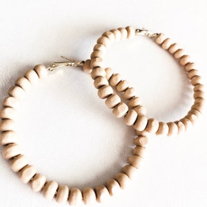 May include: A pair of large hoop earrings made of light brown wooden beads. The earrings are simple and elegant, and would be a great addition to any wardrobe.