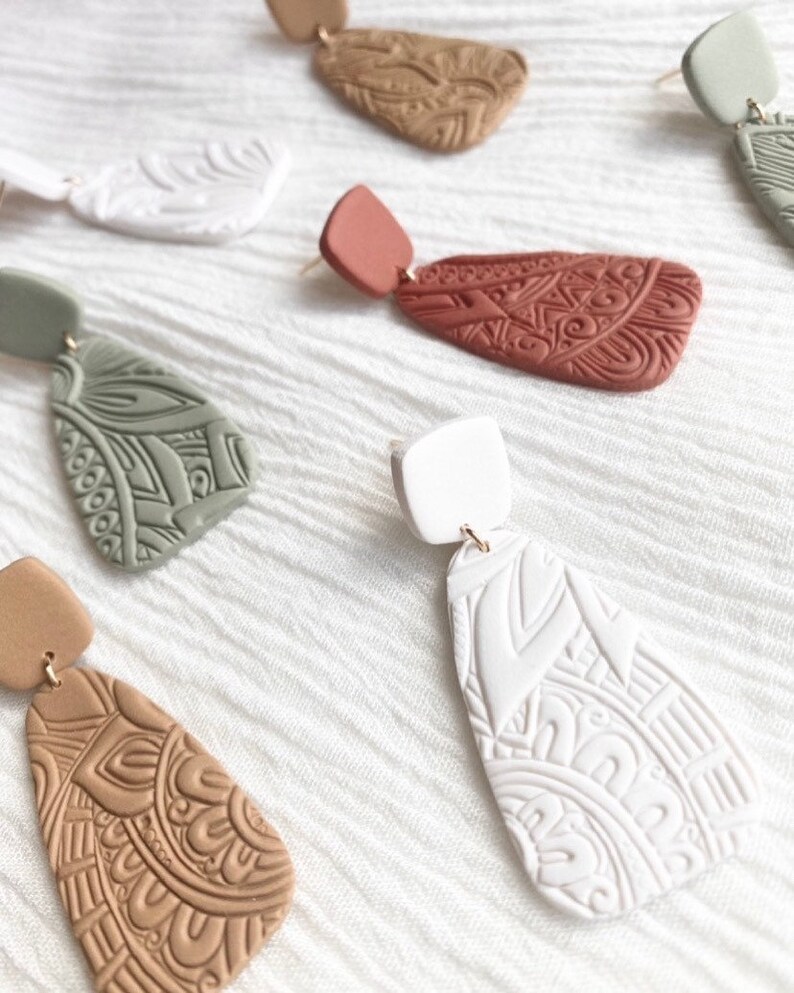 May include: Set of five pairs of dangle earrings with intricate geometric patterns. The earrings are made of clay and come in a variety of colors, including white, brown, green, and red.