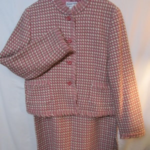 May include: A pink and white tweed jacket and skirt set with a fringe trim. The jacket has a mandarin collar and button closure. The label reads "Pendleton".