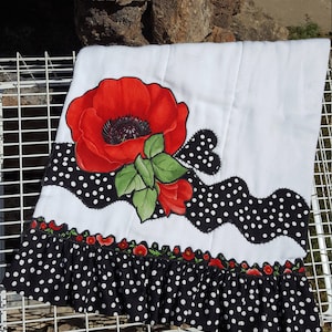 May include: White kitchen towel with a black and white polka dot ruffle trim. The towel features a hand-painted red poppy flower with green leaves.