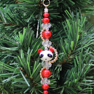 May include: A Christmas ornament featuring a panda bear charm with black and white details, surrounded by red and clear glass beads and gold accents.