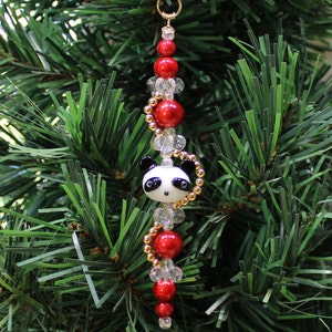 May include: A Christmas ornament featuring a panda bear charm with black eyes and a white face, surrounded by red and clear beads on a gold chain.