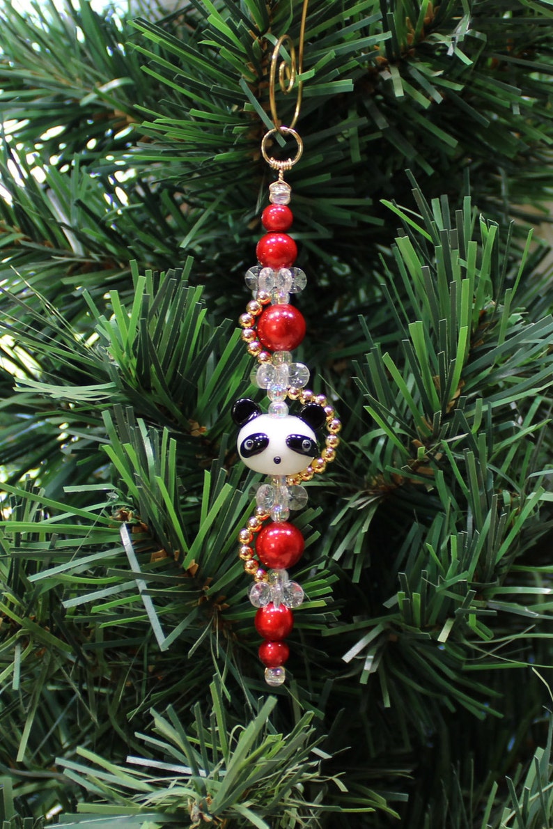 May include: A Christmas ornament featuring a panda bear charm with black eyes and a white face, surrounded by red and clear beads on a gold chain.
