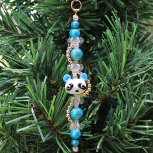 May include: A blue and white panda bear ornament with gold beads and clear crystal beads hanging from a gold wire loop.