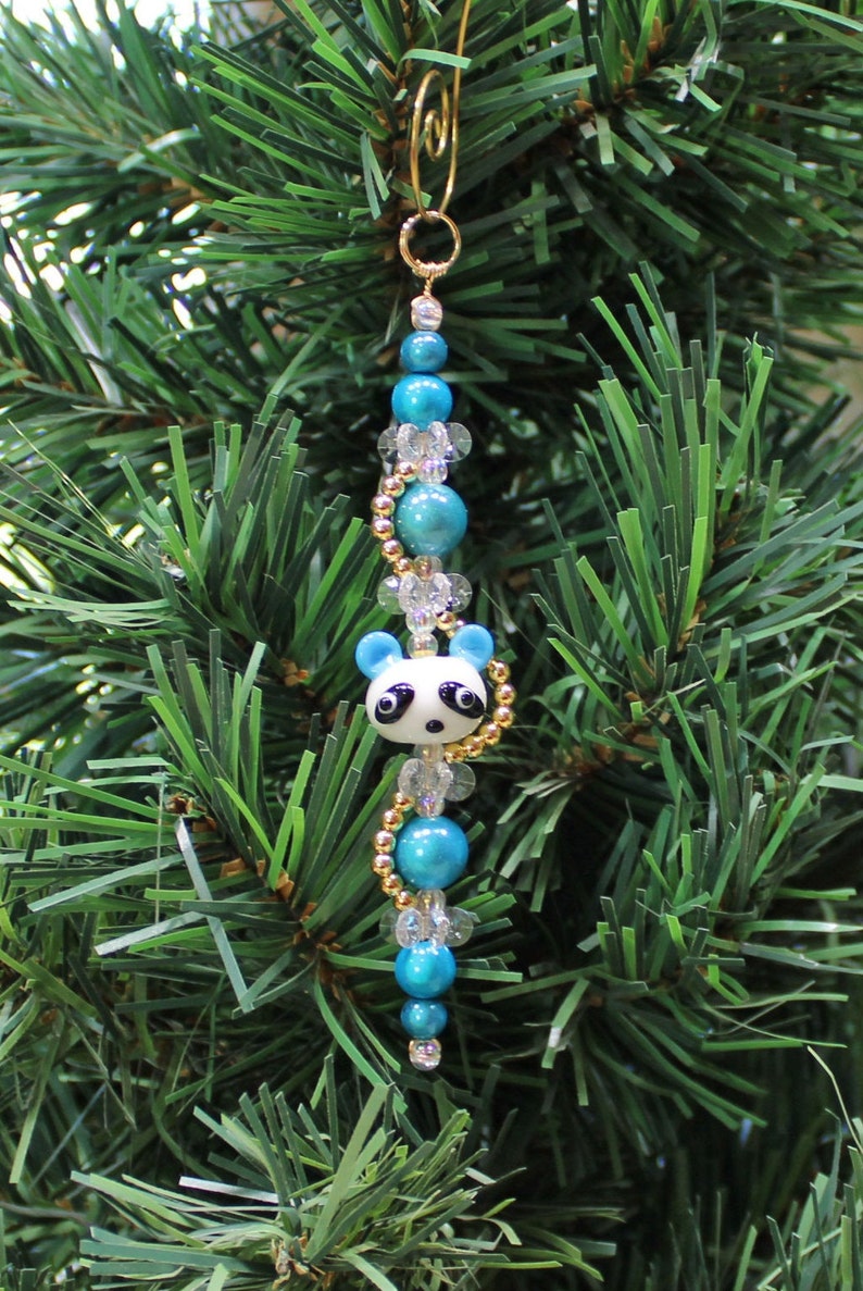 May include: A blue and white panda bear ornament with gold beads and clear crystal beads hanging from a gold wire loop.