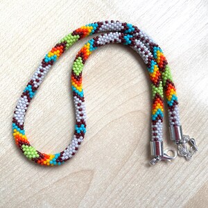 May include: A beaded necklace with a colorful pattern. The necklace features a repeating design of white, red, blue, green, orange, and yellow beads. The necklace has a silver clasp.