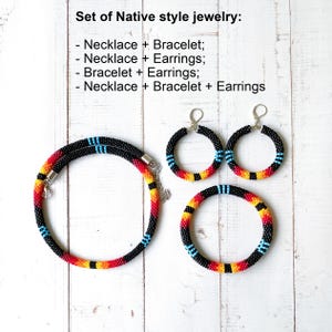 Pode incluir: Um conjunto de joias de estilo nativo, incluindo um colar, pulseira e brincos. As joias apresentam contas pretas com detalhes em vermelho, amarelo e azul. O texto "Set of Native style jewelry" está no topo.
